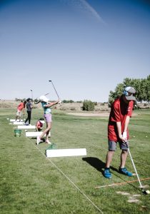 Teen golfers practicing their swings at a driving range on a sunny day.