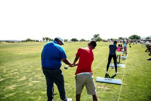 Instructor teaching golf at an outdoor course with students practicing their swings.
