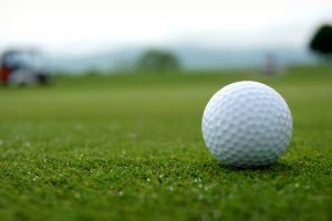 Macro shot of a golf ball on a golf course with shallow focus, highlighting the texture and setting.